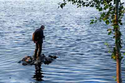 湖の岩の上に乗って釣りをしている男性の写真